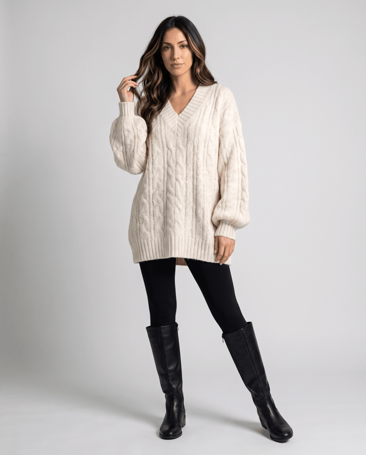 Cream Chunky Cable Knit Sweater worn by a female model with dark knee-high boots, featuring an oversized fit, chunky cable knit texture, and long sleeves.