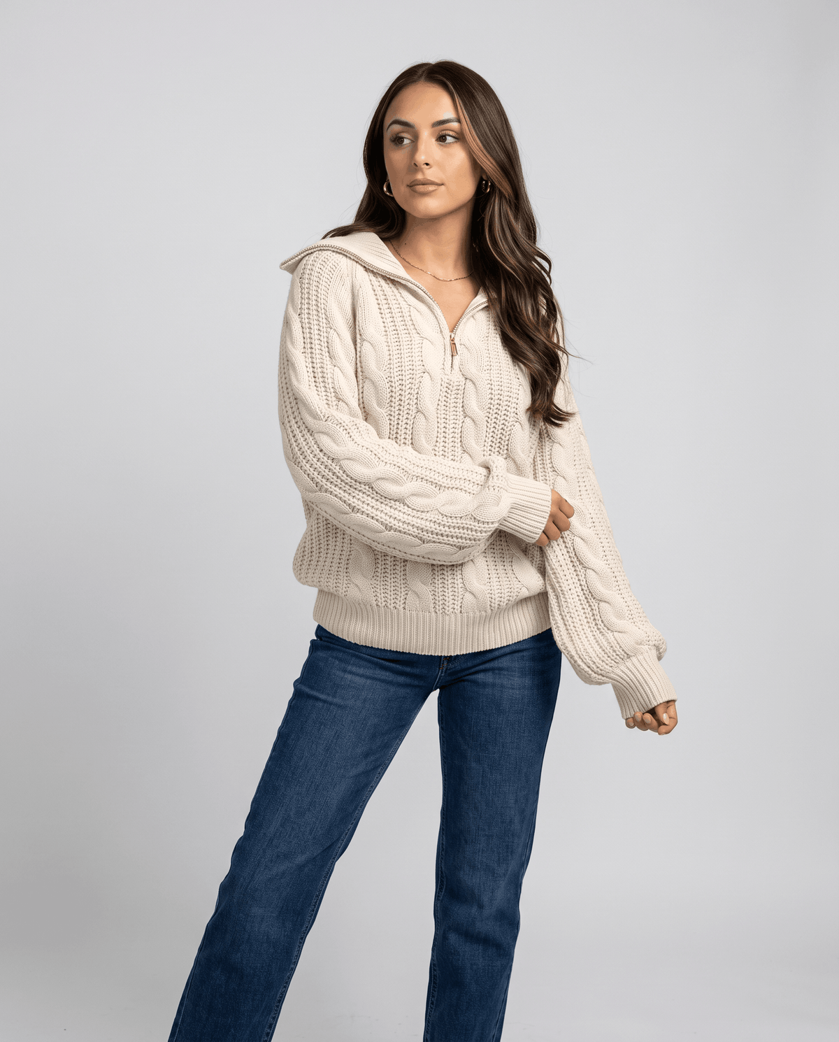 Cream Chunky Cable Knit Sweater worn by a female model with blue jeans, featuring a stand collar, half-zip front, chunky cable knit texture, and relaxed fit.