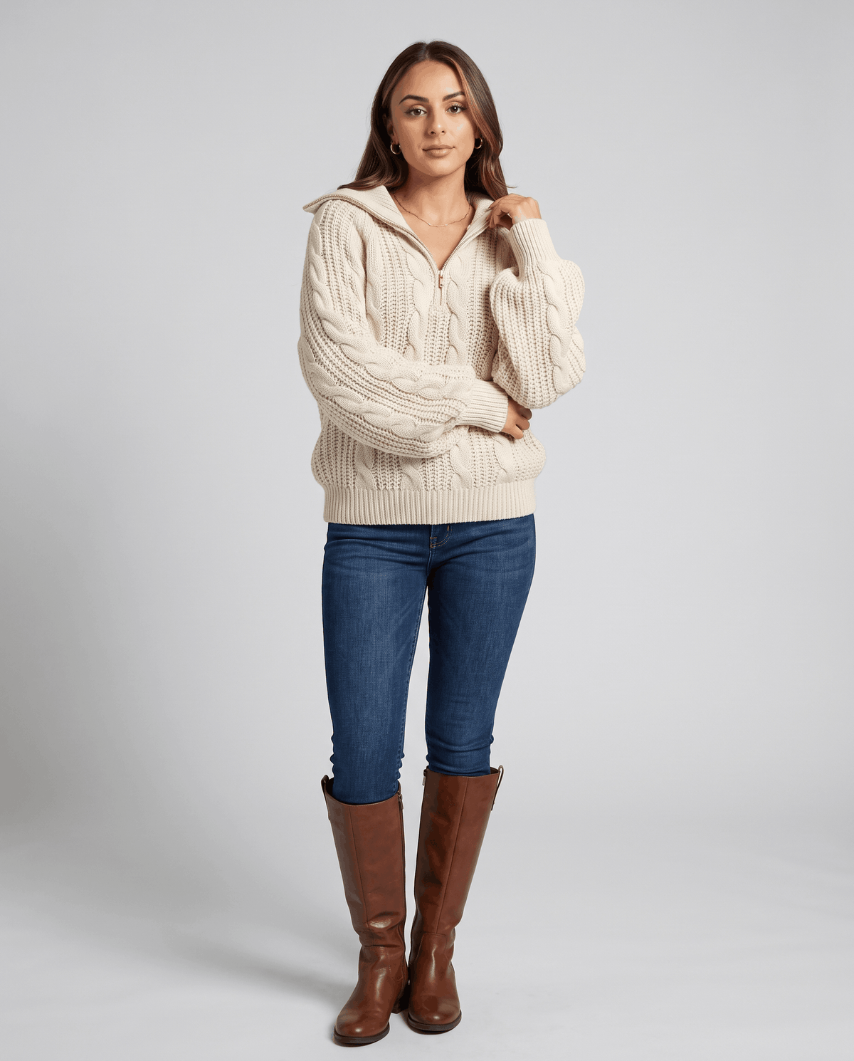 Cream Chunky Cable Knit Sweater worn by a female model with blue jeans and boots, featuring a stand collar, half-zip front, chunky cable knit texture, and relaxed fit.