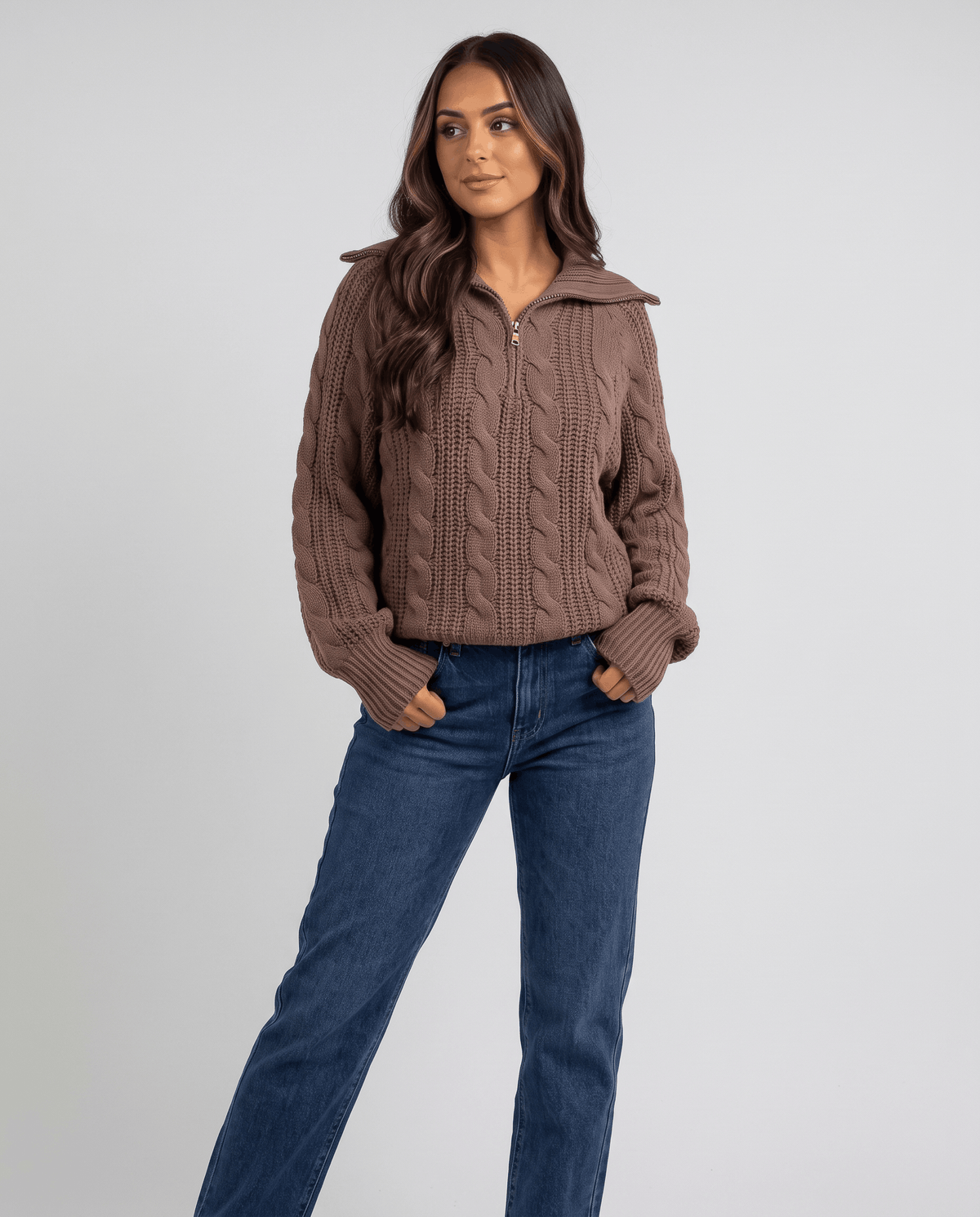 Brown Chunky Cable Knit Sweater worn by a female model with blue jeans, featuring a stand collar, half-zip front, chunky cable knit texture, and relaxed fit.