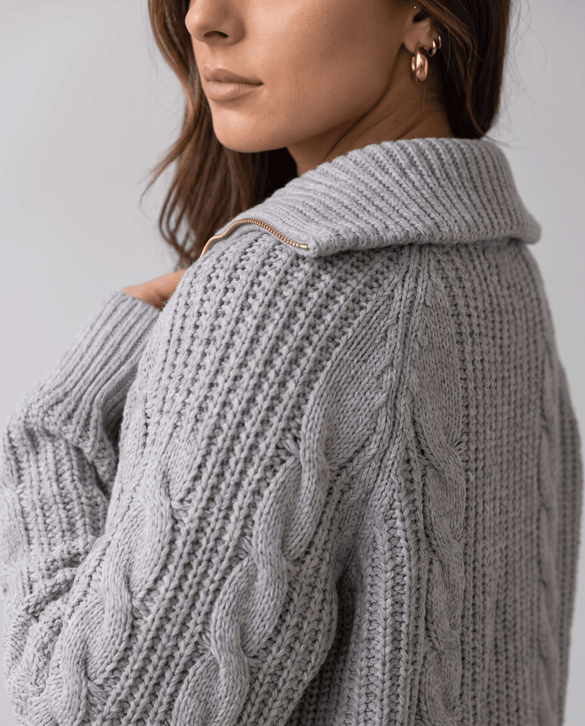 Close-up of the gray Chunky Cable Knit Sweater worn by a female model from the back, showcasing the stand collar and chunky cable knit texture.
