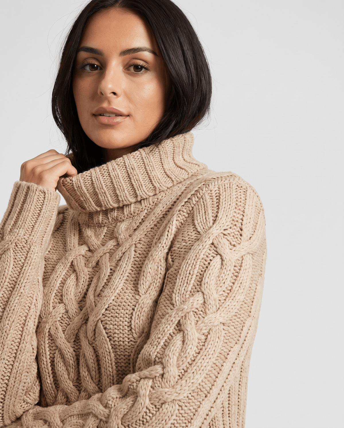 Close-up of the beige Chunky Cable Knit Sweater worn by a female model, highlighting the turtleneck collar, chunky cable knit texture, and ribbed trim.