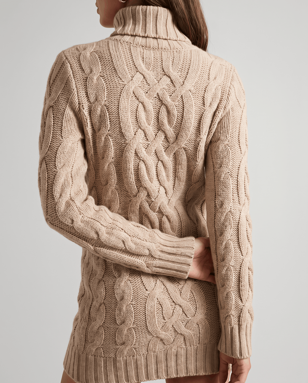 Beige Chunky Cable Knit Sweater worn by a female model from the back, showcasing the cable knit texture, turtleneck collar, long sleeves, and ribbed hem.
