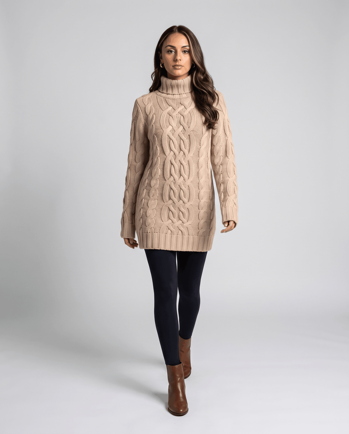 Beige Chunky Cable Knit Sweater worn by a female model with dark pants and boots, featuring a turtleneck, textured cable knit pattern, long sleeves, and ribbed trim.