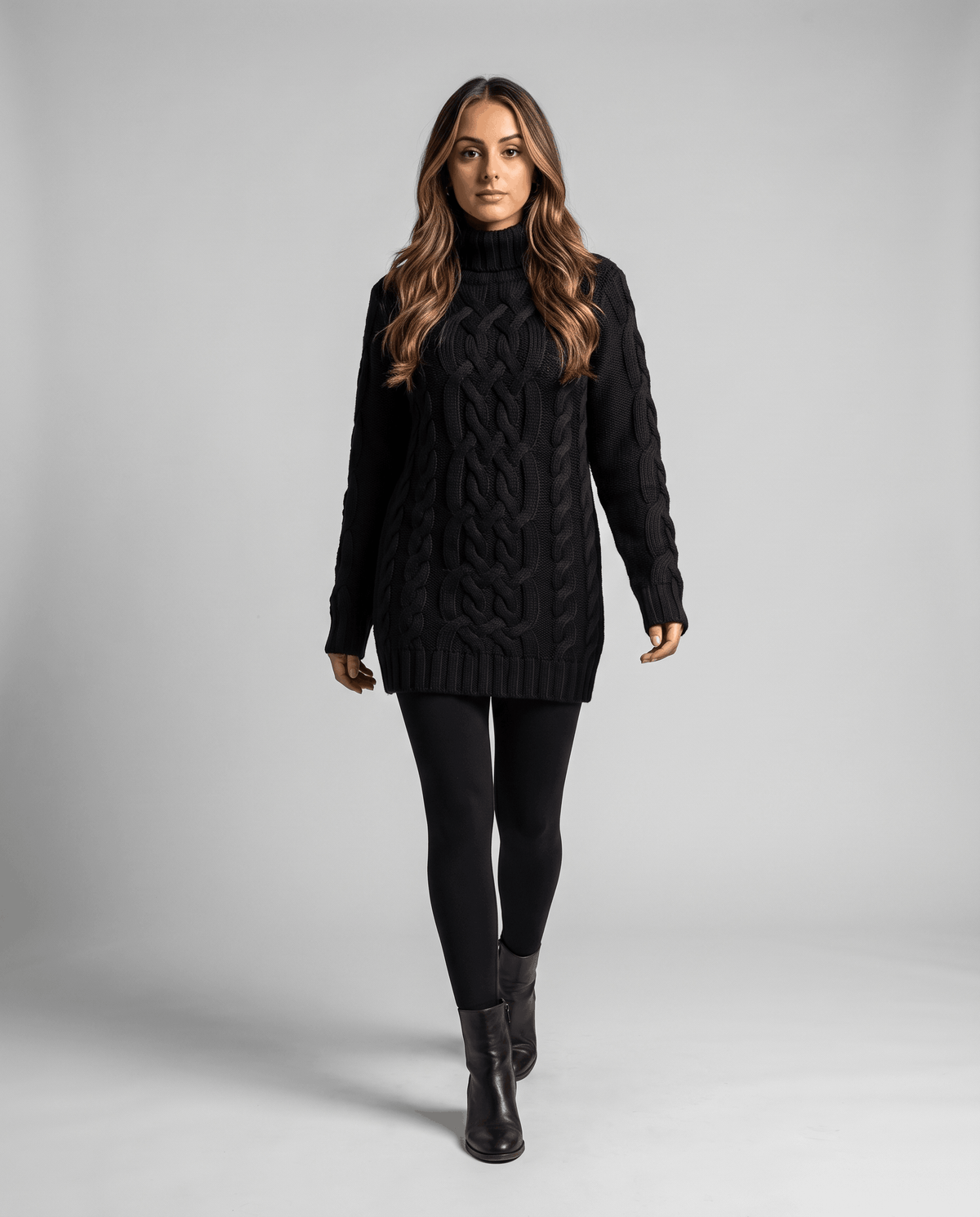 Black Chunky Cable Knit Sweater worn by a female model with black leggings and boots, featuring a turtleneck, textured cable knit pattern, long sleeves, and ribbed trim.
