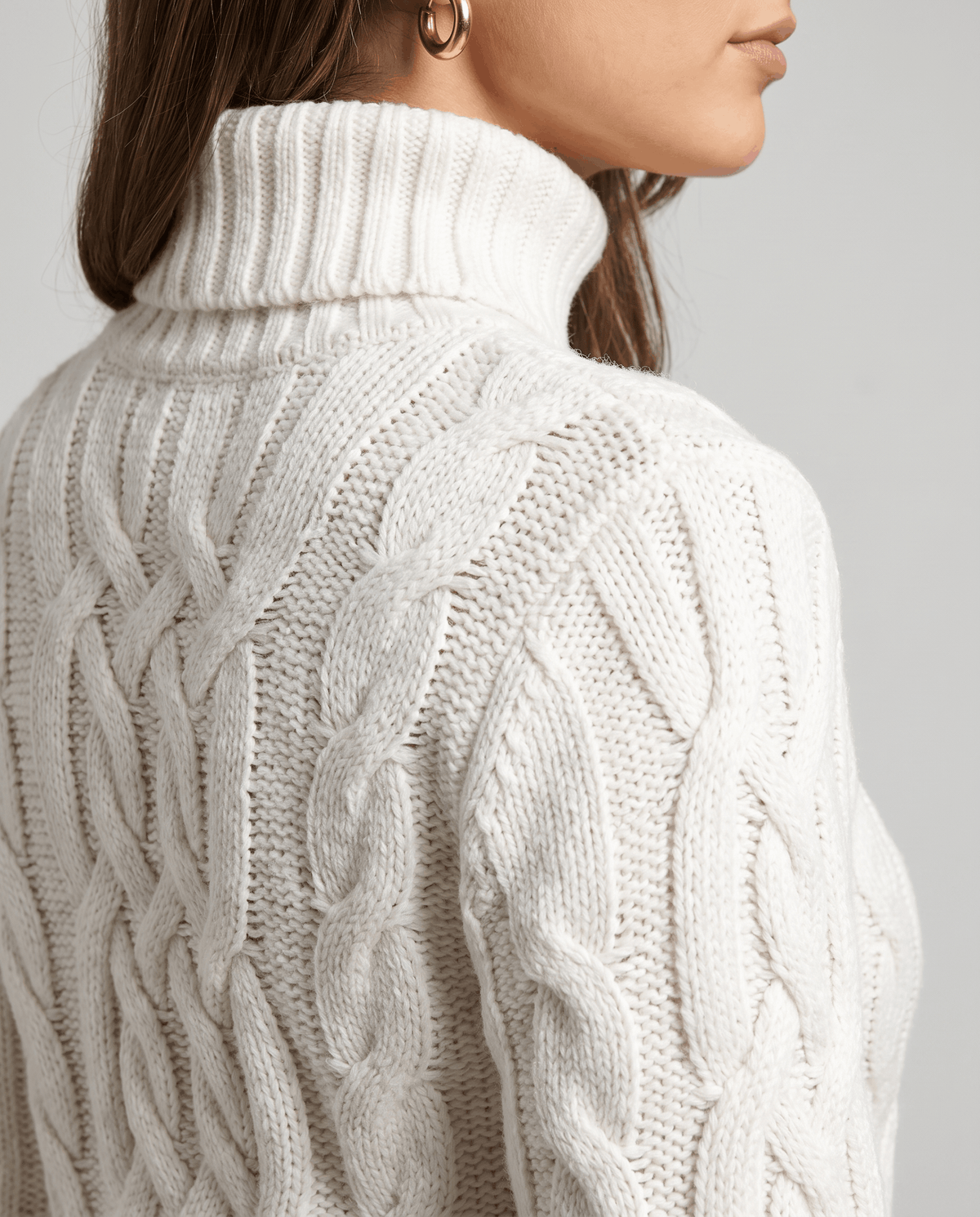 Close-up of the white Chunky Cable Knit Sweater worn by a female model from the back, highlighting the cable knit texture, turtleneck collar, and ribbed hem.