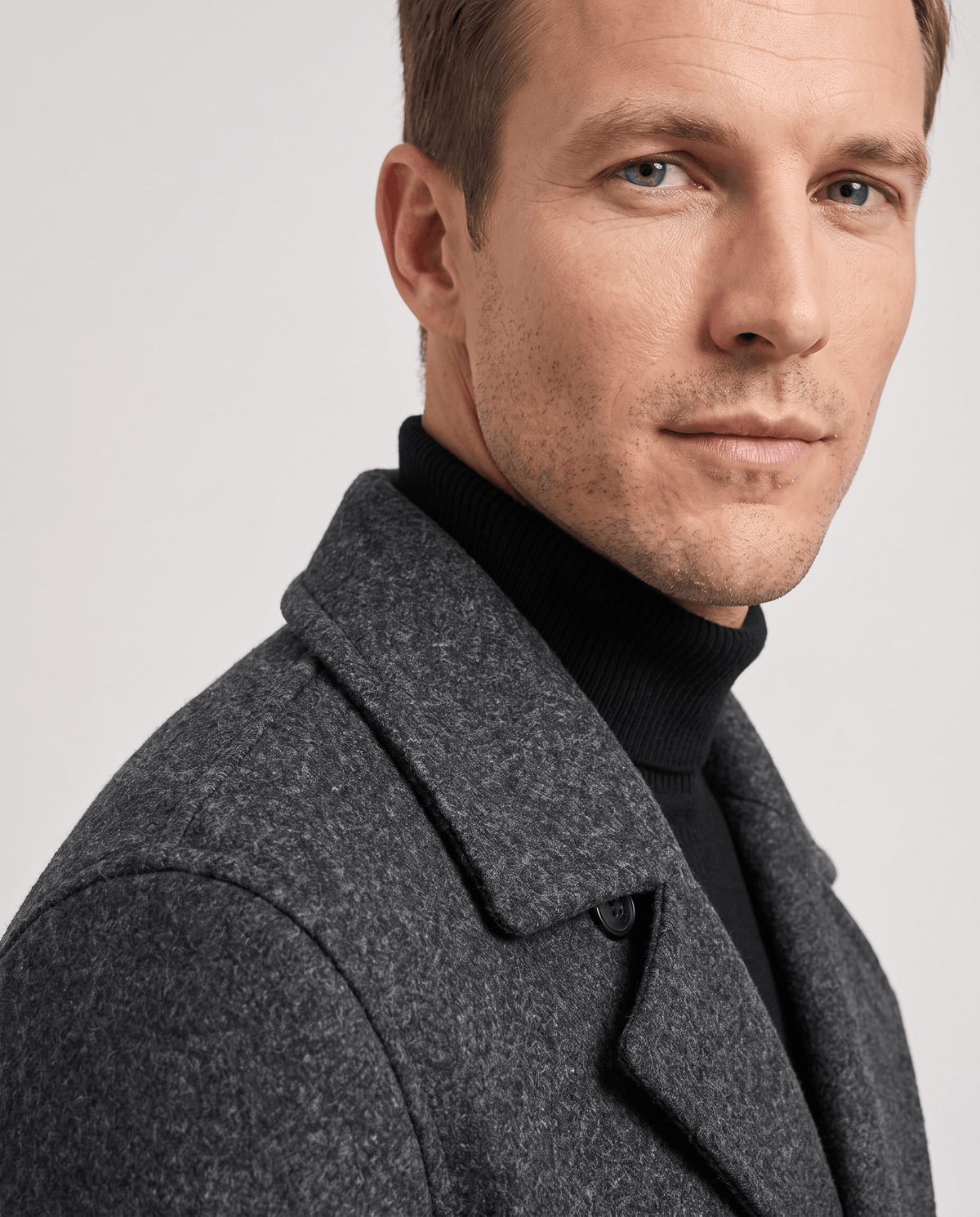 Close-up of a man wearing a gray double-breasted trench coat, showing the tailored lapels and structured collar