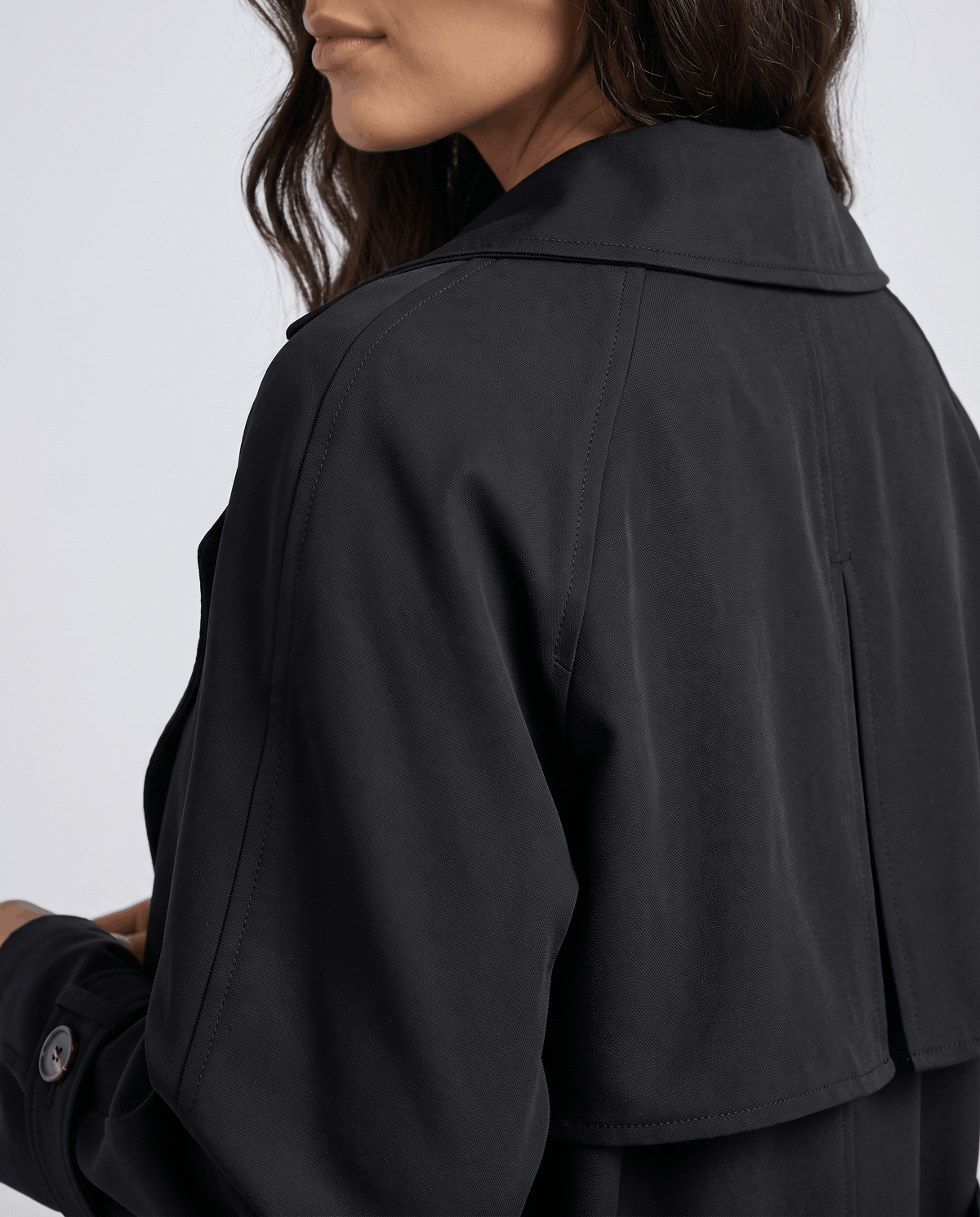A woman wearing a black classic trench coat, shown from the back, highlighting the structured lapel collar