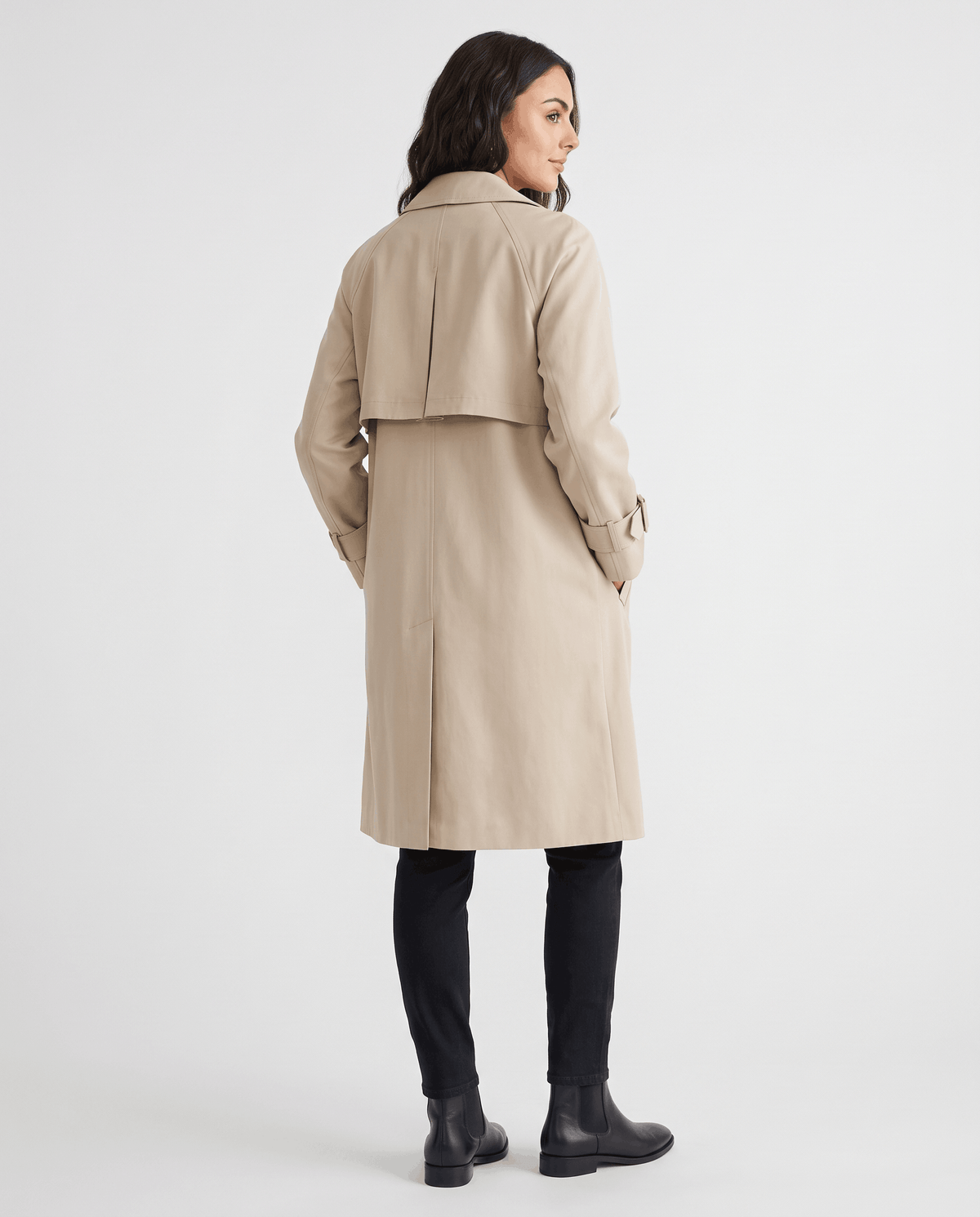 A woman wearing a beige classic trench coat with a lapel collar and double-breasted button closure, shown from the back