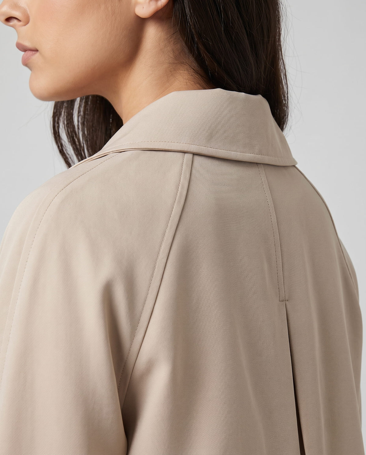 Close-up of a woman wearing a beige classic trench coat, showing the lapel collar and button closure