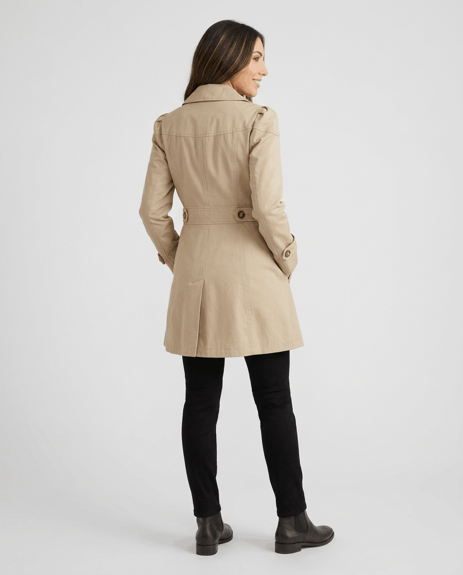 A woman wearing a cream classic trench coat with a lapel collar, button front, and adjustable cuffs, back view
