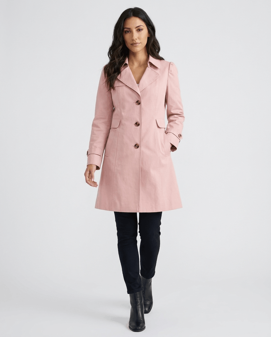 A woman wearing a pink classic trench coat with a lapel collar, button front, and adjustable cuffs
