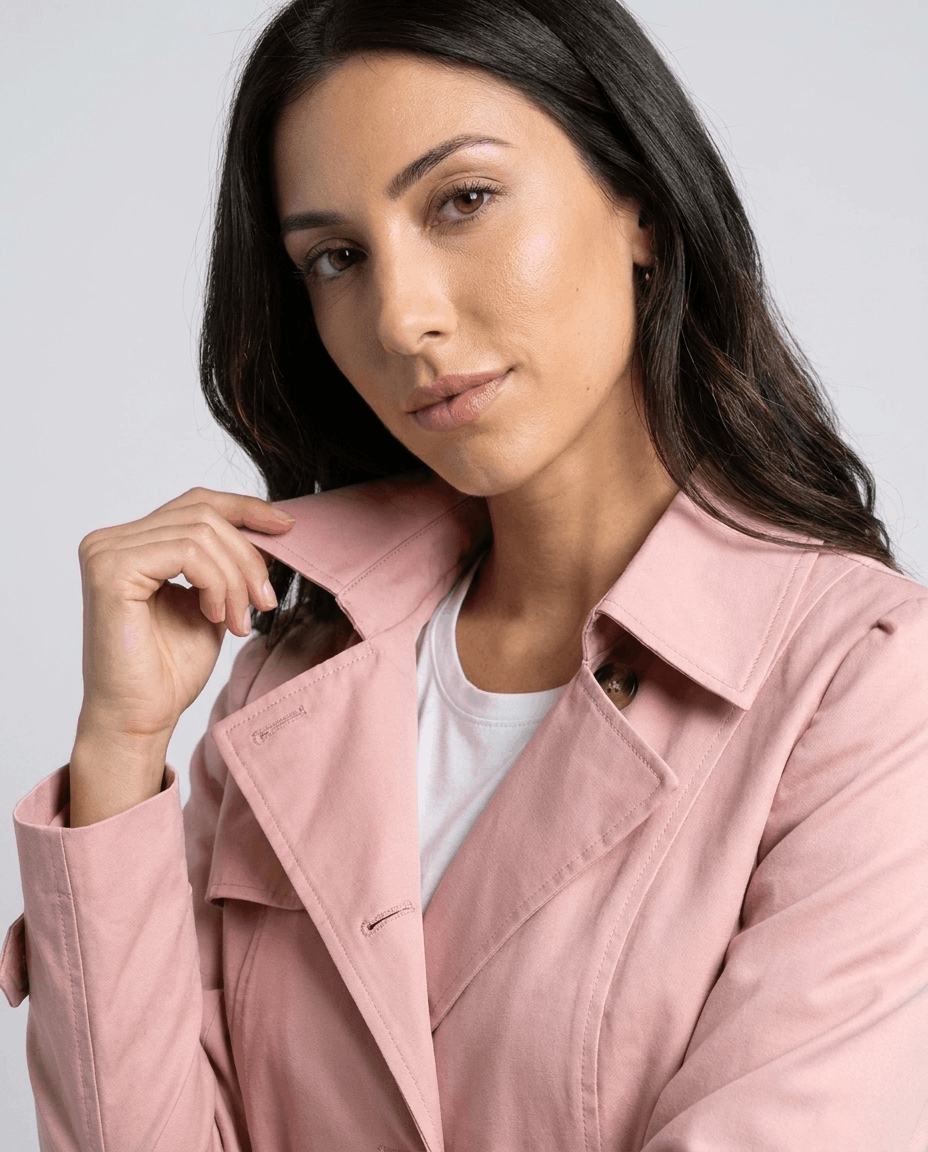Close-up of a woman wearing a pink classic trench coat, showing the lapel collar and button front
