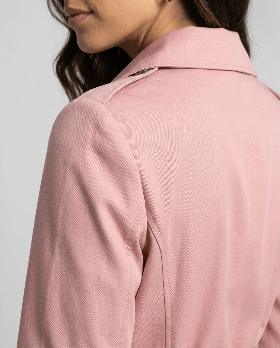 Close-up of a woman wearing a pink classic trench coat, showing the back detail and structured fit