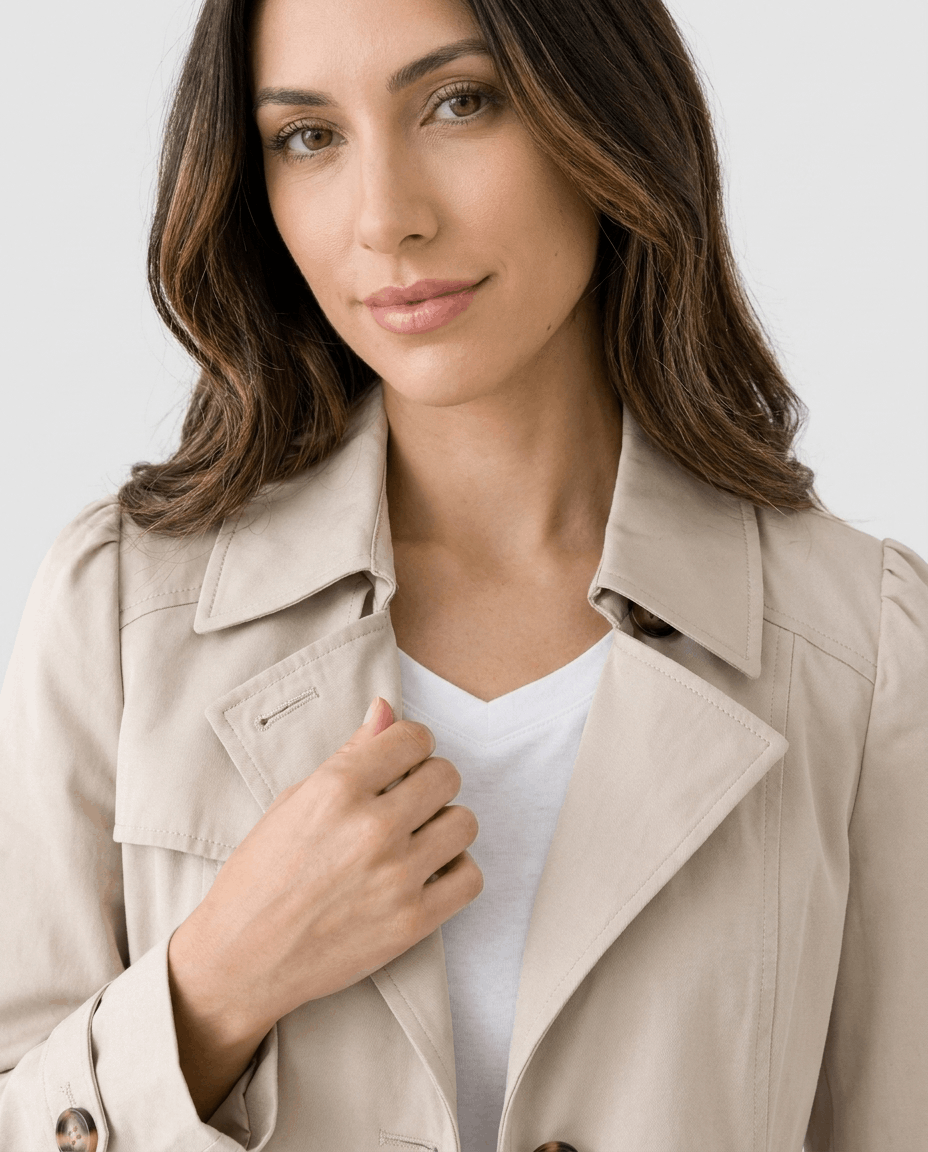 A woman wearing a cream classic trench coat with a lapel collar and button front, close-up view