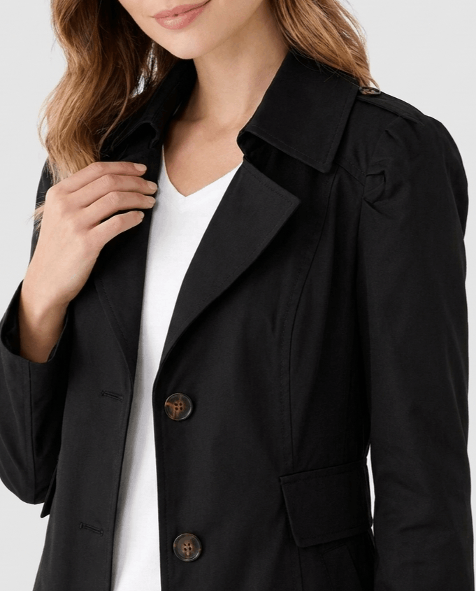 A woman wearing a black classic trench coat with a lapel collar and button front, close-up view