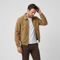 Male model wearing a tan suede-style bomber jacket over a white T-shirt and dark brown trousers.