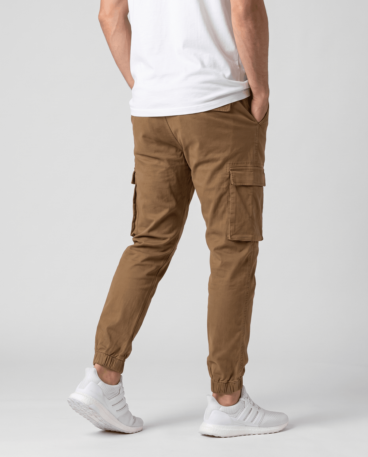 A man wearing brown cotton cargo jogger pants with a tapered fit and utility pockets, shown from the back