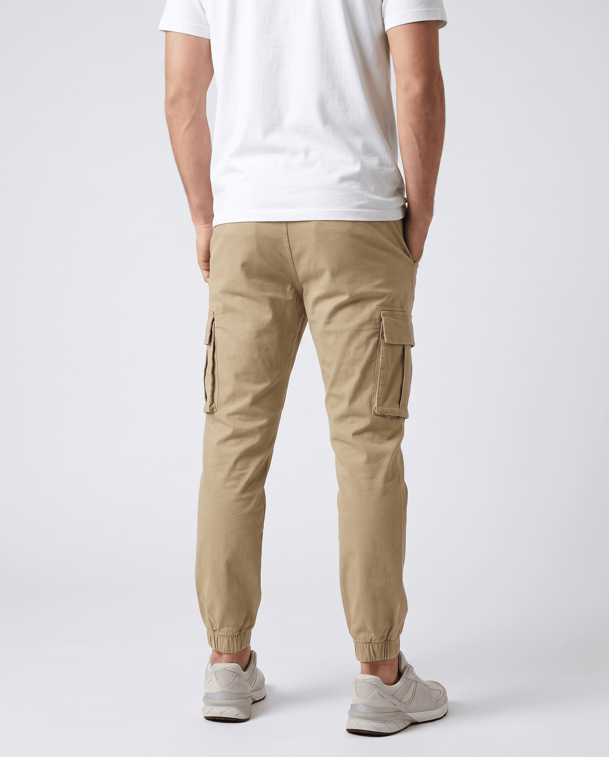 A man wearing khaki cotton cargo jogger pants with a tapered fit and utility pockets, shown from the back