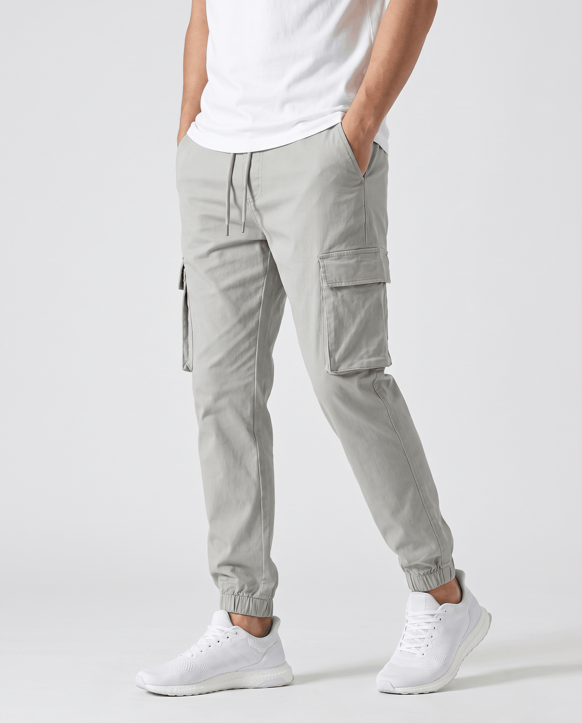 A man wearing light gray cotton cargo jogger pants with a tapered fit and utility pockets, shown from the side