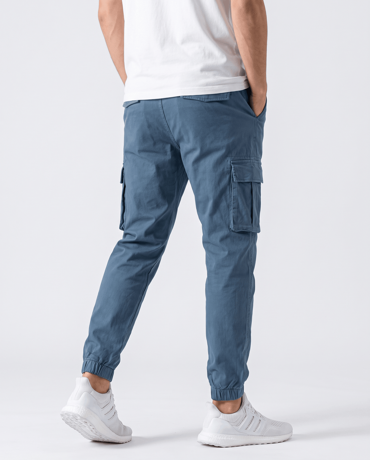 A man wearing blue cotton cargo jogger pants with a tapered fit and utility pockets, shown from the back