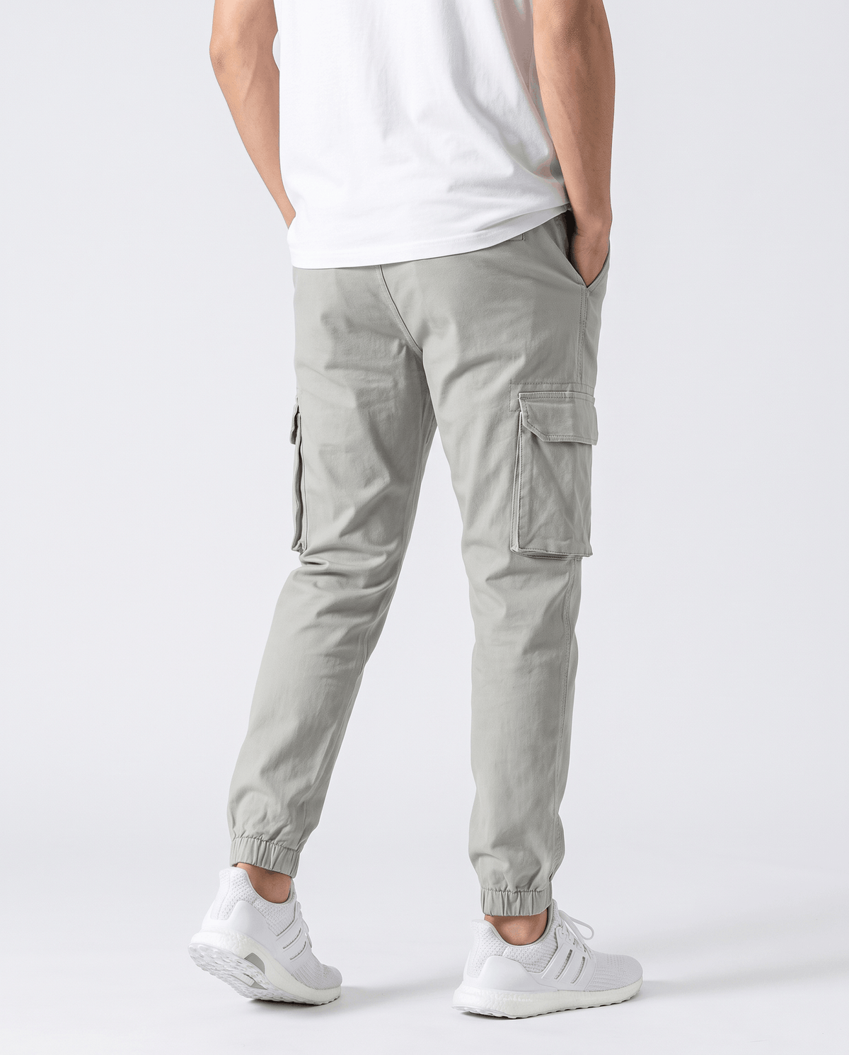 A man wearing light gray cotton cargo jogger pants with a tapered fit and utility pockets, shown from the back