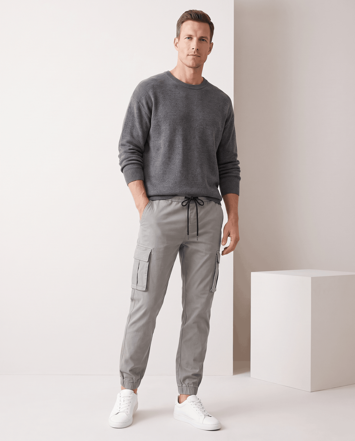 A man wearing gray cotton cargo jogger pants with a tapered fit and utility pockets, standing indoors