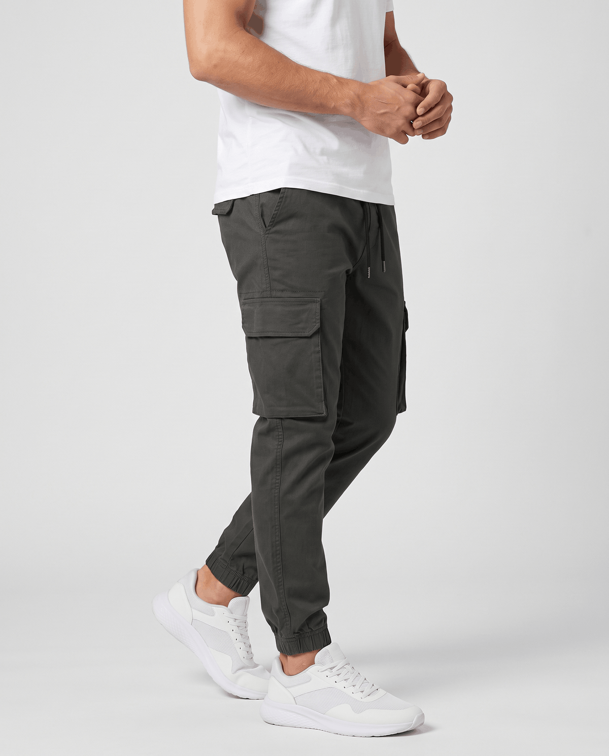 A man wearing dark olive cotton cargo jogger pants with a tapered fit and utility pockets, shown in side view