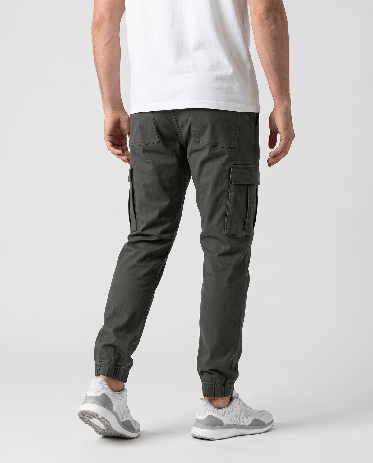 A man wearing dark gray cotton cargo jogger pants with a tapered fit and utility pockets, shown from the back