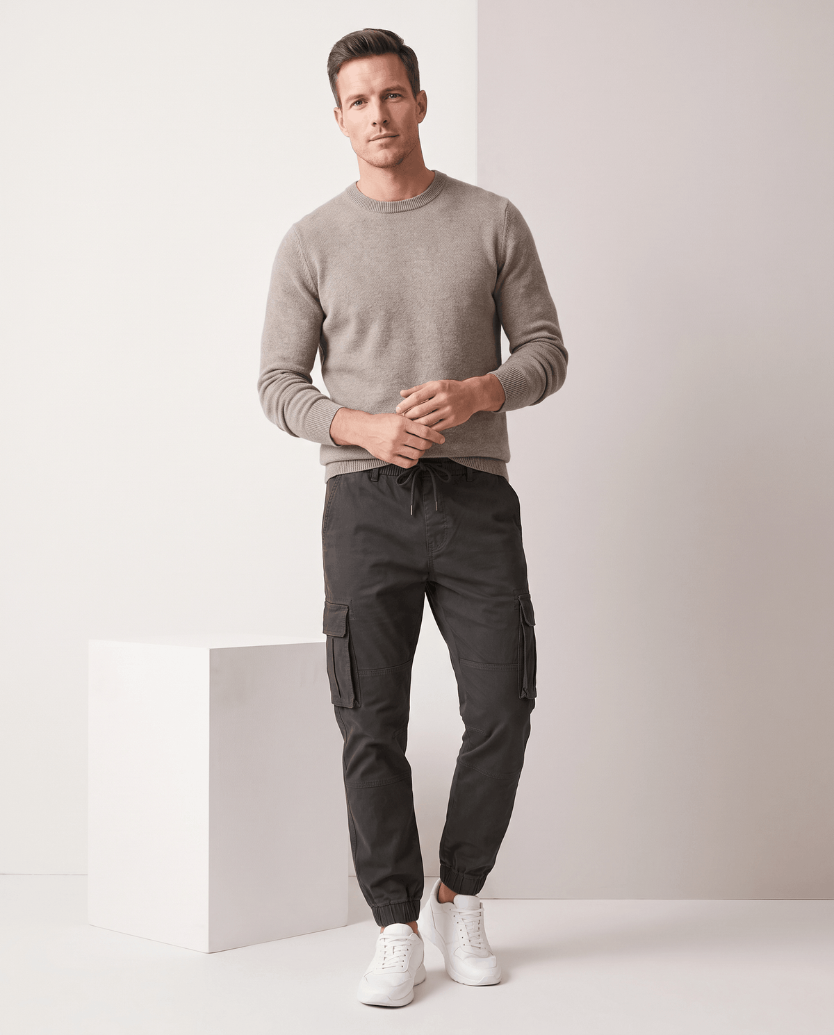 A man wearing dark gray cotton cargo jogger pants with a tapered fit and utility pockets, standing indoors