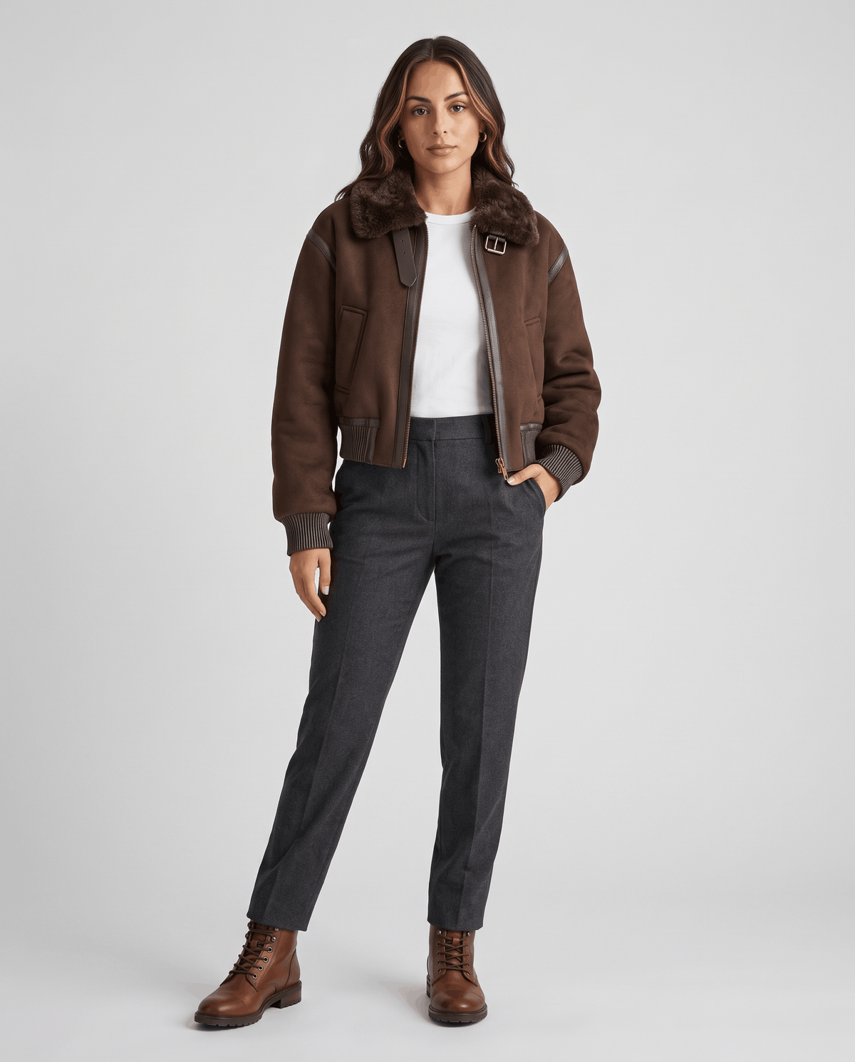 A woman wearing a cropped dark brown shearling bomber jacket with a plush collar and ribbed trim, full-length view