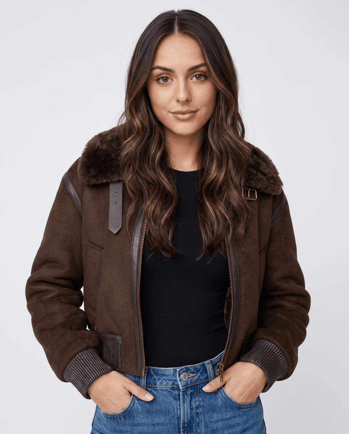 A woman wearing a cropped dark brown shearling bomber jacket with a plush collar and ribbed trim, front view