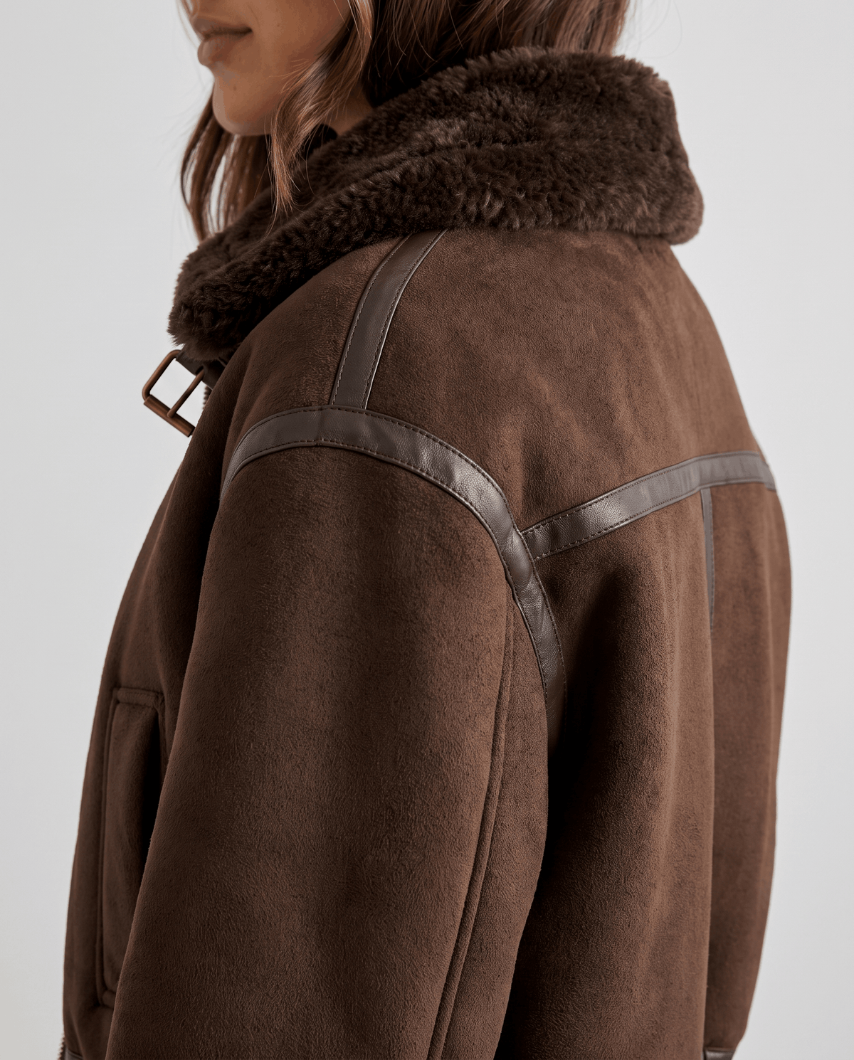 Close-up of a dark brown cropped shearling bomber jacket showing the plush collar and back detail