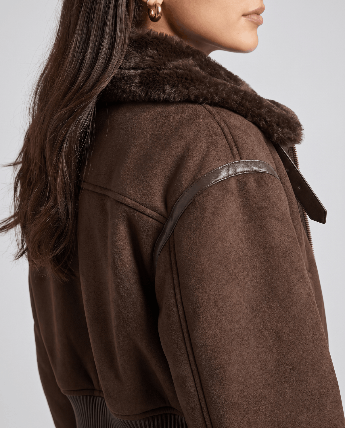 Close-up of a dark brown cropped shearling bomber jacket showing the plush collar and ribbed trim