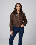 A woman wearing a cropped dark brown shearling bomber jacket with a plush collar and ribbed trim