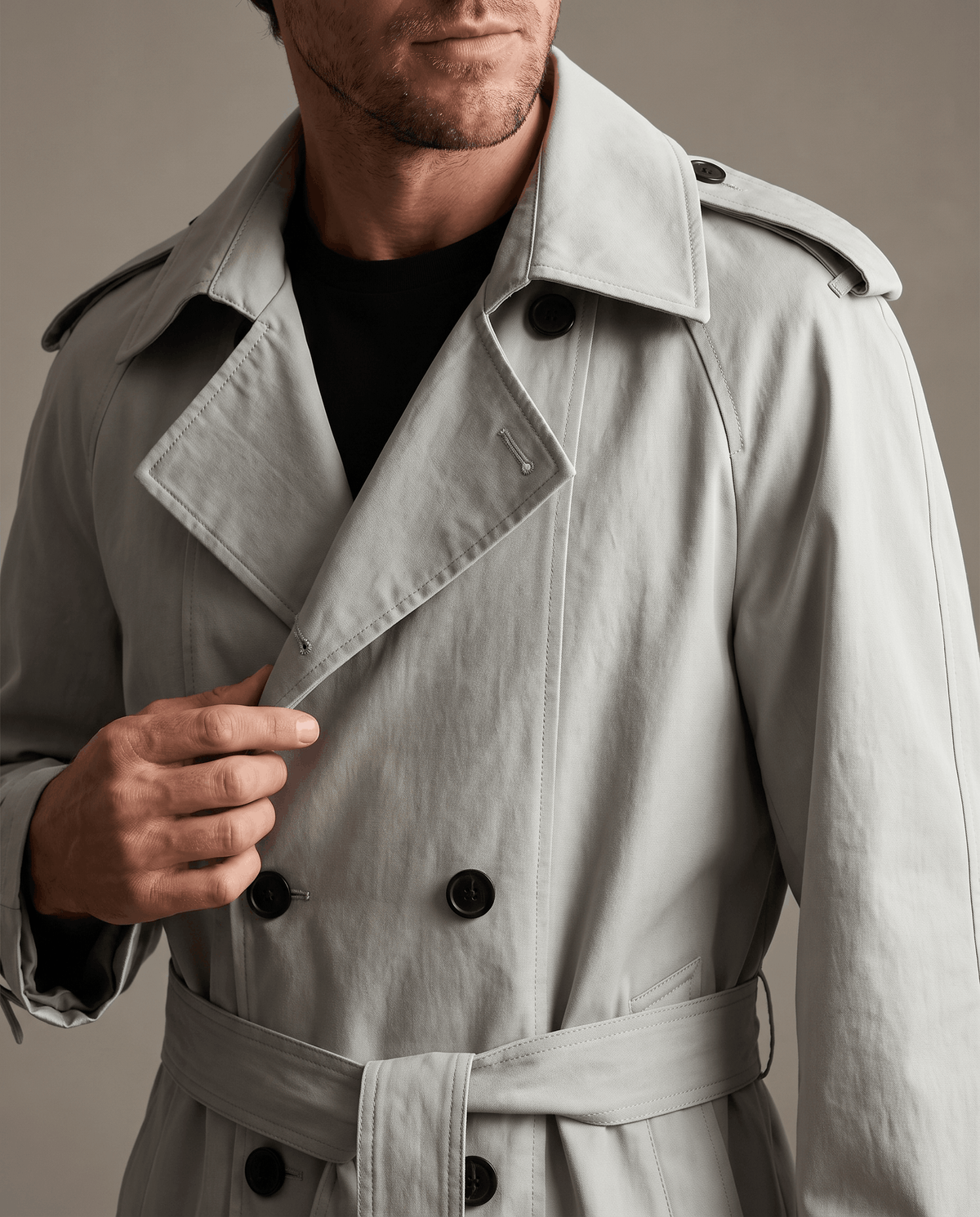 Close-up of a man wearing a light gray double-breasted trench coat, showing the wide lapels, button front, and belted waist