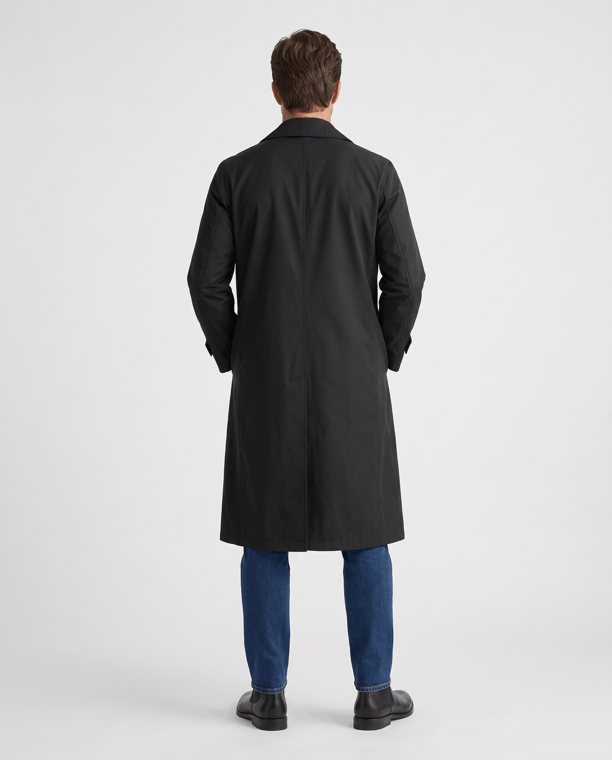 A man wearing a black double-breasted trench coat with a belted waist and adjustable cuffs, shown from the back