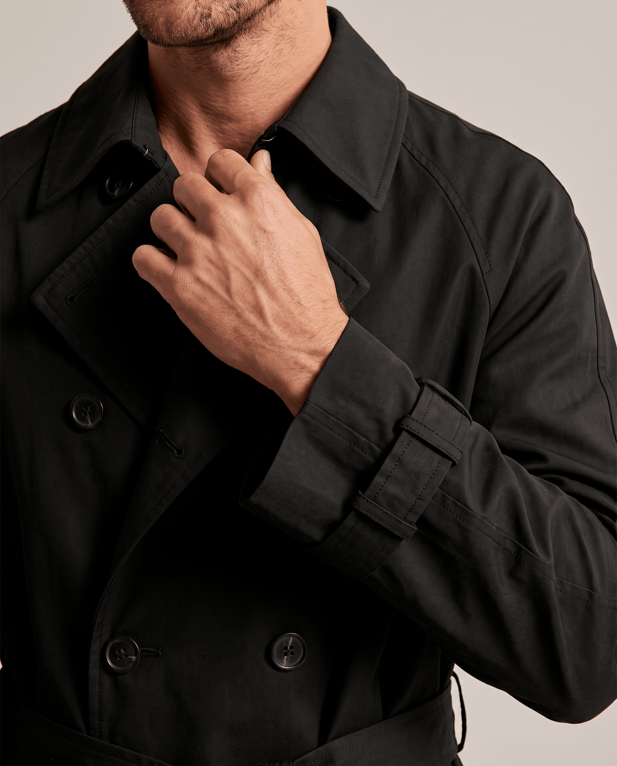 Close-up of a man wearing a black double-breasted trench coat, showing the lapels, button front, and collar
