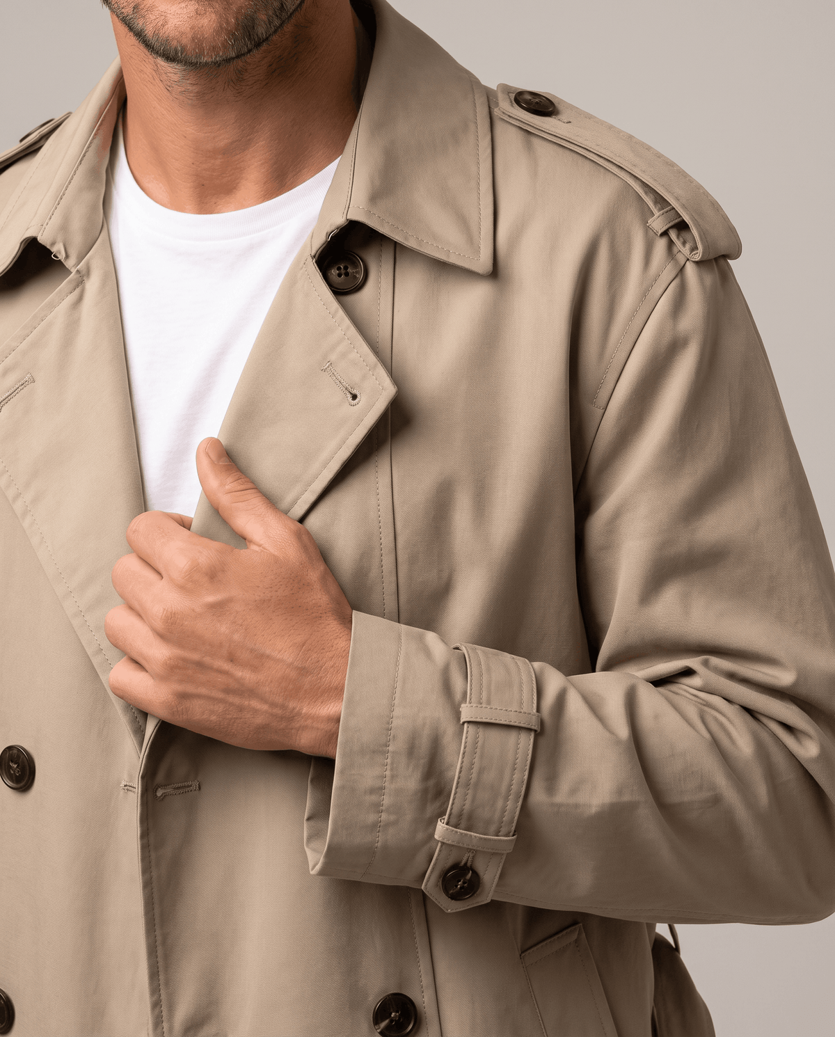 Close-up of a man wearing a beige double-breasted trench coat, showing the lapels, button front, and adjustable cuff