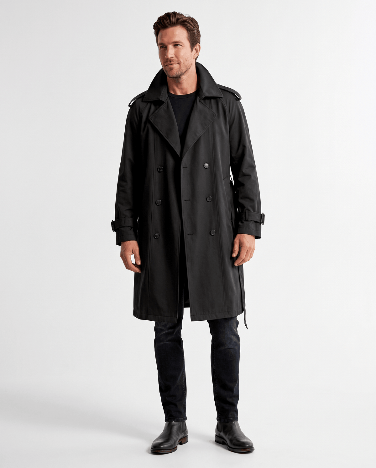 A man wearing a black double-breasted trench coat with a belted waist and adjustable cuffs