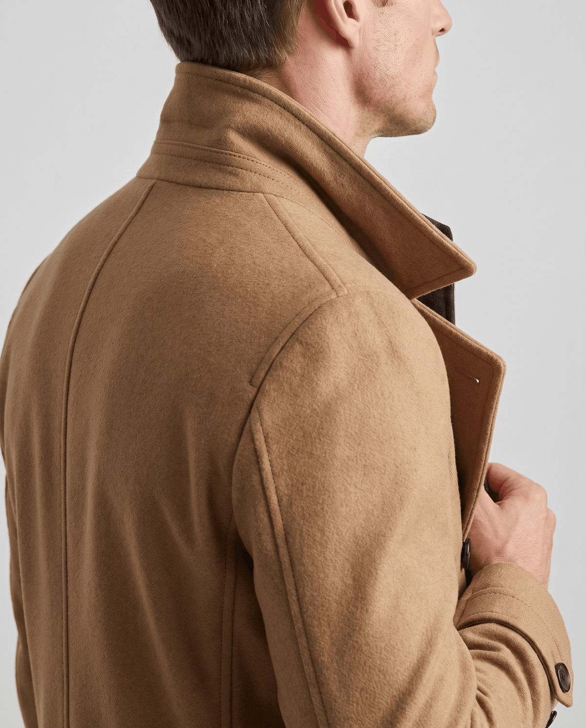 Close-up of a man wearing a camel double-breasted trench coat, showing the notched lapel and structured shoulder