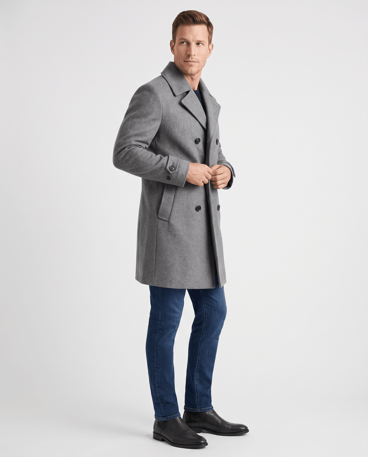 A man wearing a gray double-breasted trench coat with a longline fit, notched lapel, and structured shoulders, side view