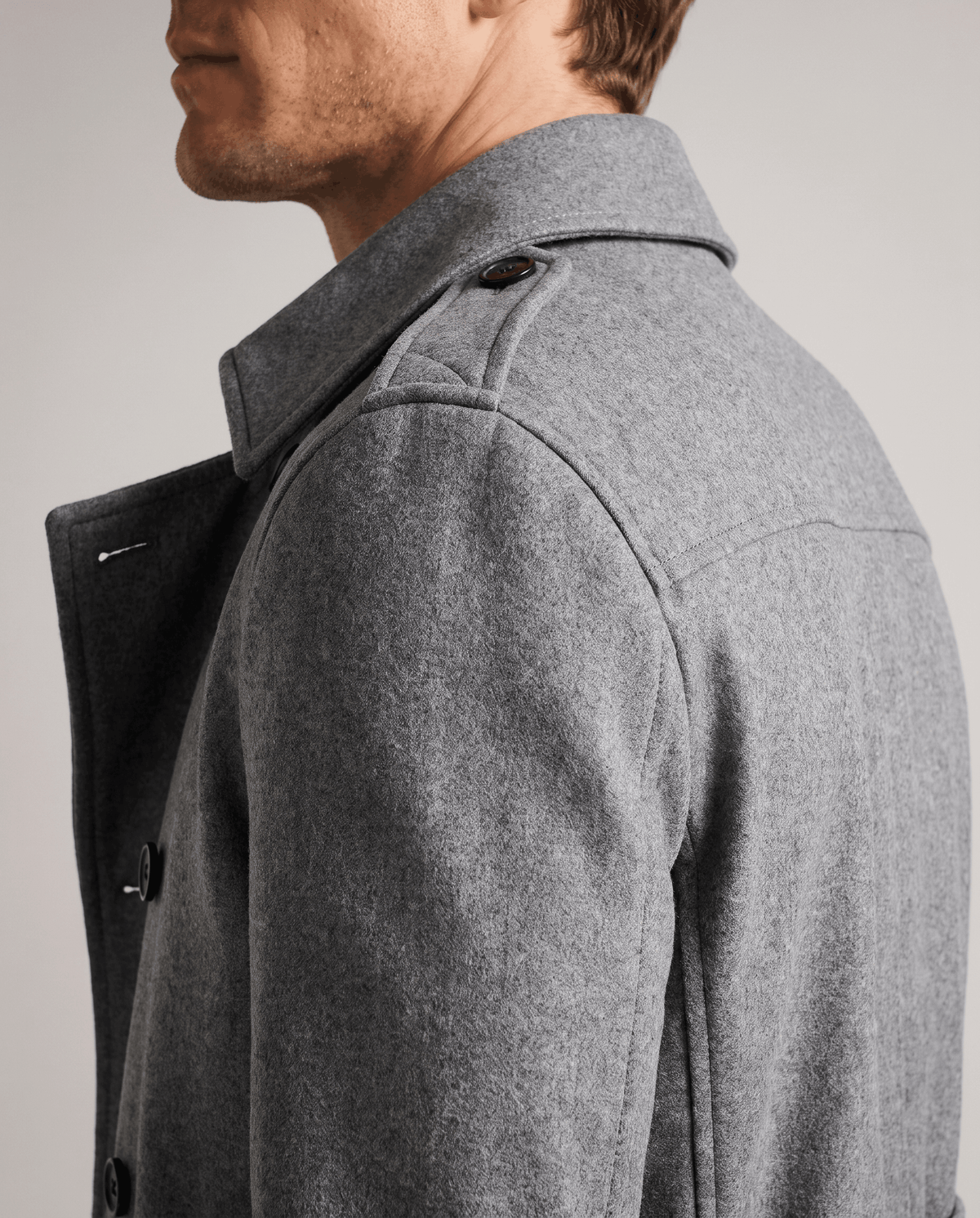 Close-up of a man wearing a gray double-breasted trench coat, showing the notched lapel and structured shoulder