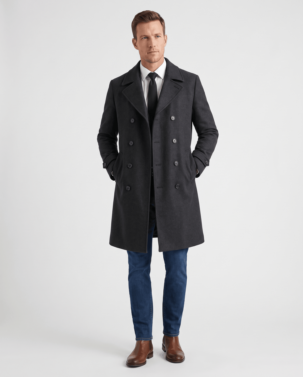 A man wearing a black double-breasted trench coat with a longline fit, notched lapel, and structured shoulders