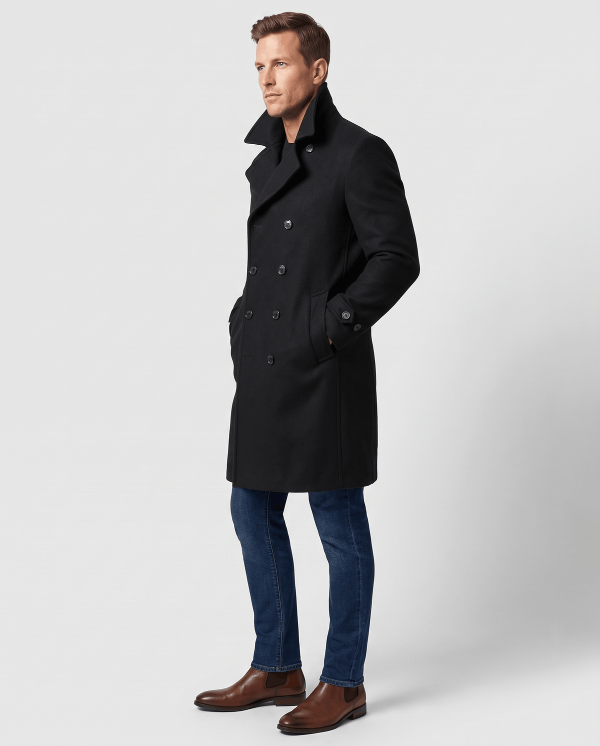 A man wearing a black double-breasted trench coat with a longline fit, notched lapel, and structured shoulders, side view