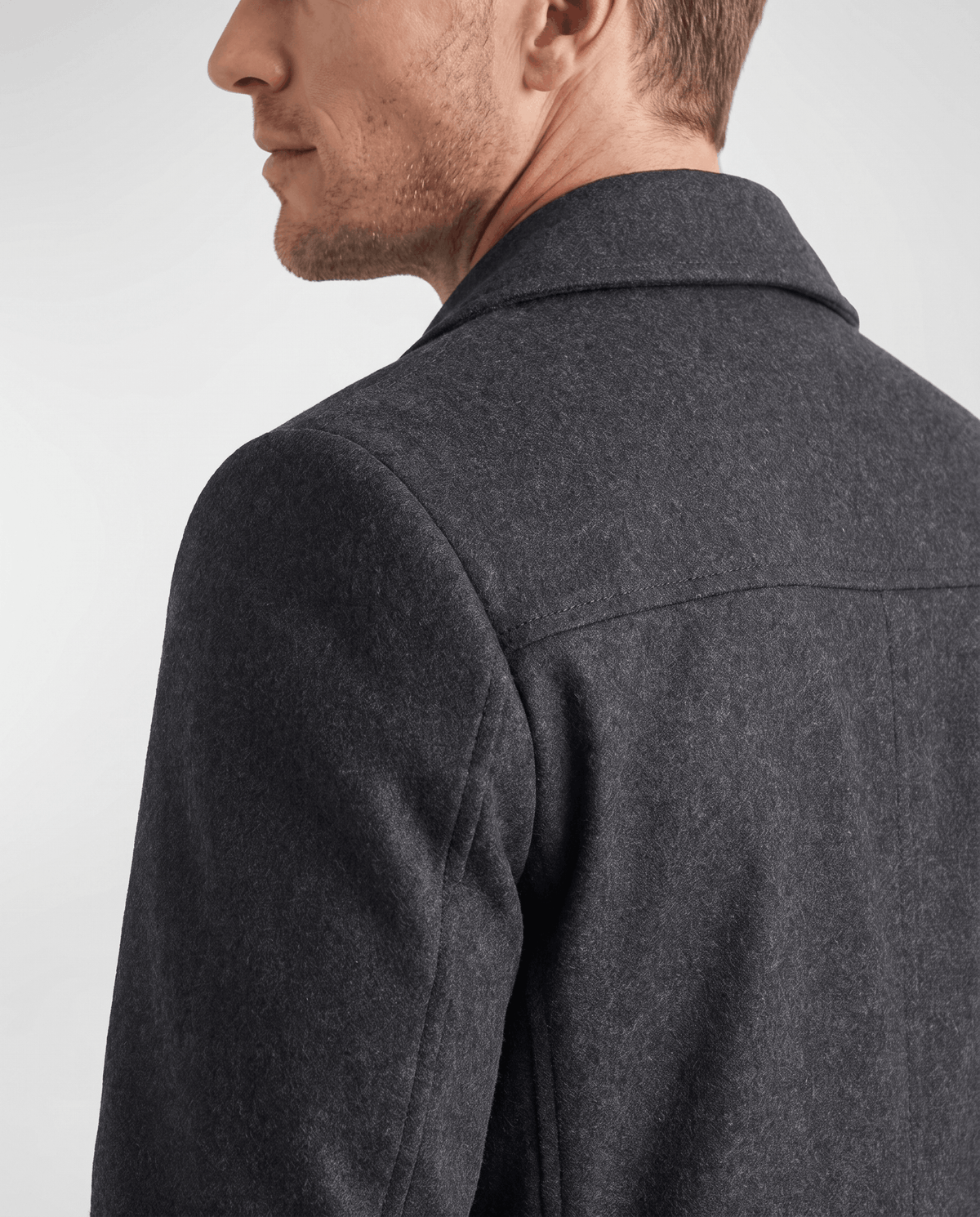 Close-up of a man wearing a black double-breasted trench coat, showing the notched lapel and structured shoulder