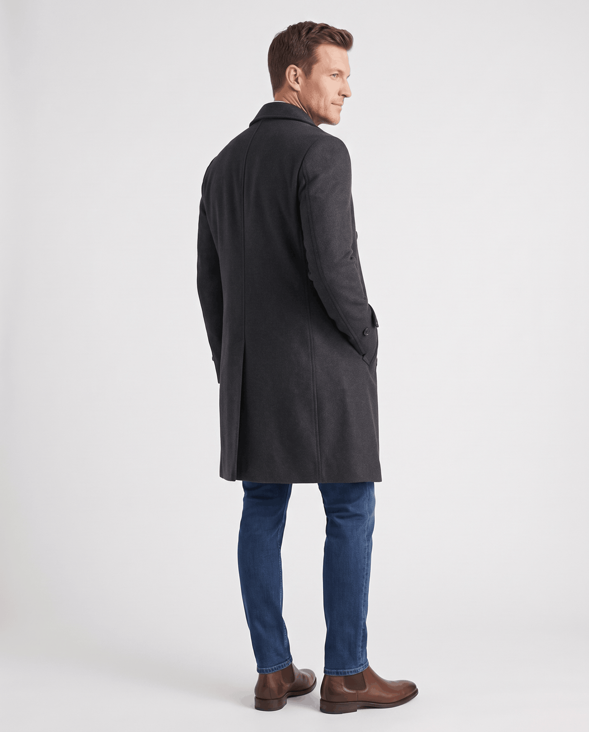 A man wearing a black double-breasted trench coat with a longline fit and structured shoulders, back view
