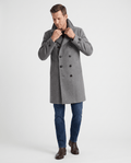 A man wearing a gray double-breasted trench coat with a longline fit, notched lapel, and structured shoulders