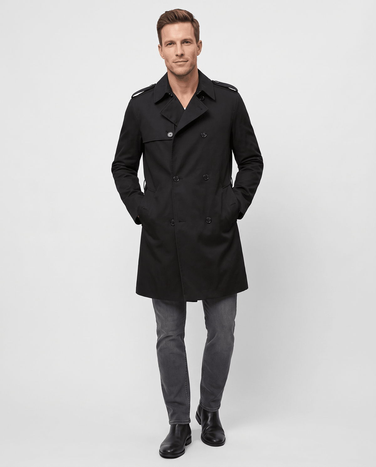 A man wearing a black double-breasted trench coat with a mid-length fit, notched lapel, and adjustable cuffs, full-body view
