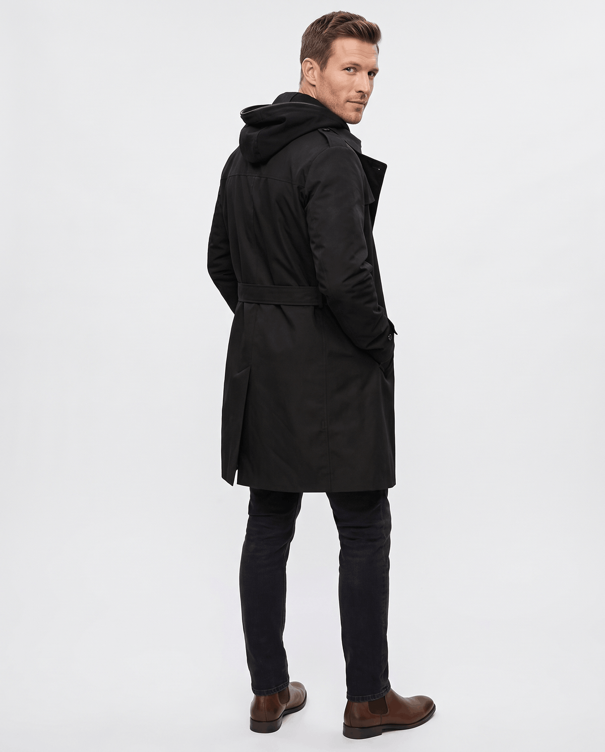 A man wearing a black double-breasted trench coat with a mid-length fit, notched lapel, and adjustable cuffs, back view